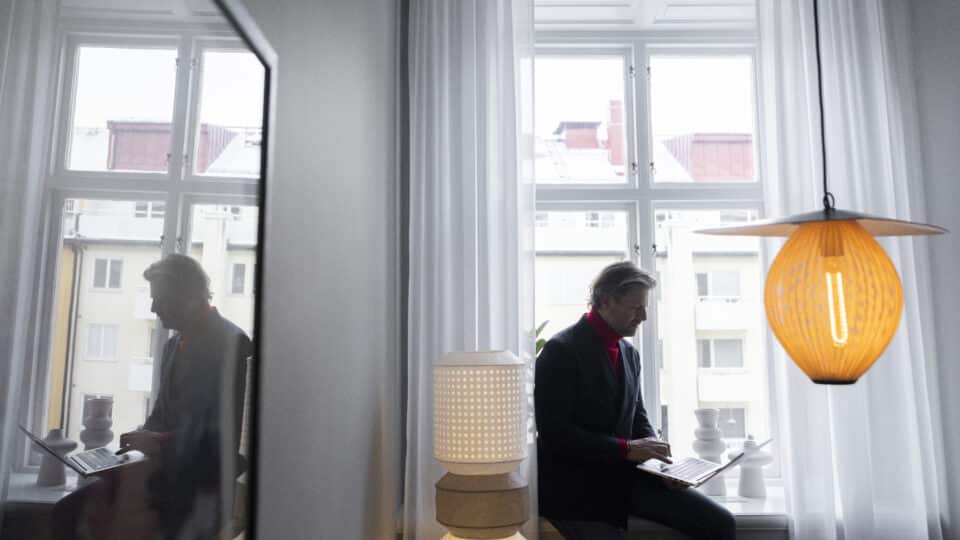 Person sitter vid ett fönster och arbetar koncentrerat på sin laptop i en ljus miljö med reflektioner i glasytor, symboliserande öppenhet och insyn kopplat till lönetransparensdirektivet.